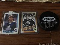 Photo showing Wendel Clark rookie card, 'Marquee Legend' hockey card, and signed National Sports puck on wooden surface.