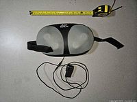 Top view of massage pillow with strap extended, adapter and tape measure showing scale