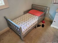 Full view of gray toddler bed with mattress from side angle