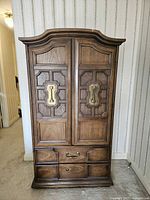 Front view of closed armoire showing paneled doors, brass escutcheons, lower drawers