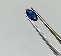 Close view of marquise sapphire held by tweezers showing shape and royal blue color
