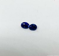 Two dark blue oval sapphires on white background
