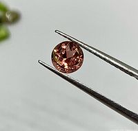 Close-up of faceted salmon/olive tourmaline held in tweezers