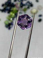 Front view of hexagon-cut purple amethyst held by tweezers