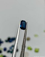 Emerald-cut royal blue sapphire held in tweezers front view