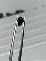 Pear shape dark blue sapphire held by tweezers