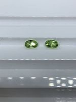 Two green oval peridot stones on white background