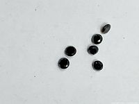 Six small round faceted black diamonds on white background