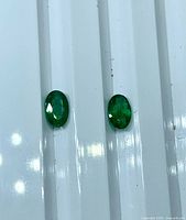 Two oval emeralds on white surface