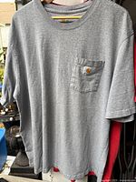 Front view heather gray Carhartt pocket T-shirt on hanger, red shirt partially behind
