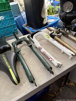 Array of bicycle parts on table including two Supercycle saddles and three forks