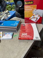 Overall lot showing laminating pouch box, ruled sheets pack, notebooks stack, memo pads, sticky notes