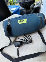 Front view of blue JBL Xtreme speaker with shoulder strap and power adapter