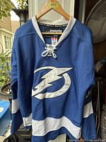 Front view of blue Tampa Bay Lightning jersey on hanger showing bolt logo and lace-up collar