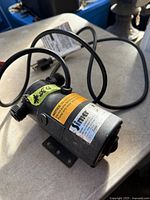Overall view of Simer portable utility pump showing housing, labels, hose ports, power cord and mounting bracket
