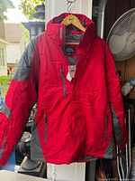 Front view of red and gray Tri-Mountain winter coat hanging on hanger with tags visible