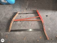 Full view of wooden frame buck saw showing red arm, blade, and tension wire