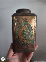 Front view of gold-tone tin showing oval bird graphic and lid