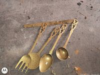 Full view of brass rack with four utensils laid below