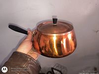 Side view of copper fondue pot with lid and black wood handle