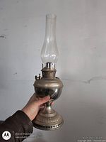 Full view of silver metal oil lamp with clear glass chimney held in hand