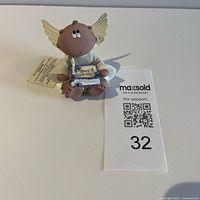 Front view of seated angel figurine, hang tag and lot card visible