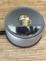 Top view of silver rotating display base showing orange and green LEDs through central lens