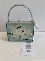 Front view of purse-shaped coin bank showing shoe motif, rhinestones, beaded handle, size reference card