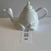 Side view of white camel-shaped ceramic teapot with lid