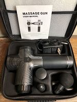 Open carrying case showing massage gun, three attachments, charger, and manual