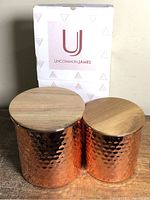 Two hammered copper canisters with wood lids alongside original Uncommon James box