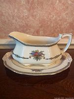 Side view of gravy boat on saucer showing floral pattern and silver trim