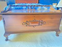 Front view of cedar chest showing carved scroll panel, spindle rail, cabriole legs