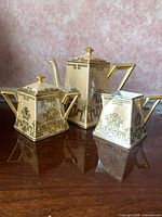 Front view of teapot, sugar bowl and creamer showing shape and gold decoration