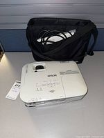 Projector front/top view with carry bag and cables visible