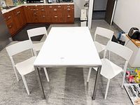 Full view of white table with metal legs and four matching white chairs