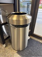 Full view of stainless steel round trash can beside door