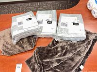 Three packaged towel sets and two faux fur throws on table