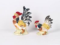 Front view of both ceramic rooster figurines, displaying size difference
