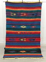 Full view of woven wool blanket hanging to show size, colour bands, geometric patterns, fringe