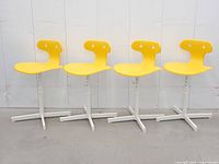 Front view of four identical yellow Ikea Molte kids chairs on white adjustable bases