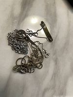 Tangled group of sterling silver chains and rectangular bar piece on marble surface