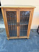 Front view of light brown MDF cabinet with closed glass doors showing arched grille design