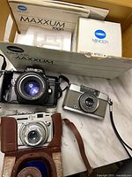 Three cameras laid out: Minolta Maxxum 7000, grey half-frame camera, Ciro 35 in case; Minolta box visible