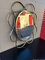 Front angled view of round mirror showing looping gold-tone metal frame and clear glass