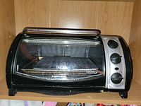 Front view of BLACK+DECKER countertop toaster oven showing glass door, three control knobs and interior tray