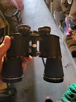 Overall view of black full-size porro-prism binoculars showing focus wheel, eyepieces, objectives and attached strap