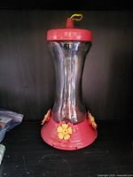 Full view of plastic hummingbird feeder showing reservoir shape, red base and lid, yellow ports, hanging loop