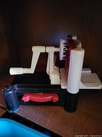 Side view of manual vegetable spiralizer showing crank, blade area, and base with red drawer