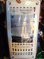 Front of sealed retail package showing Mainstays stacking utility shelf